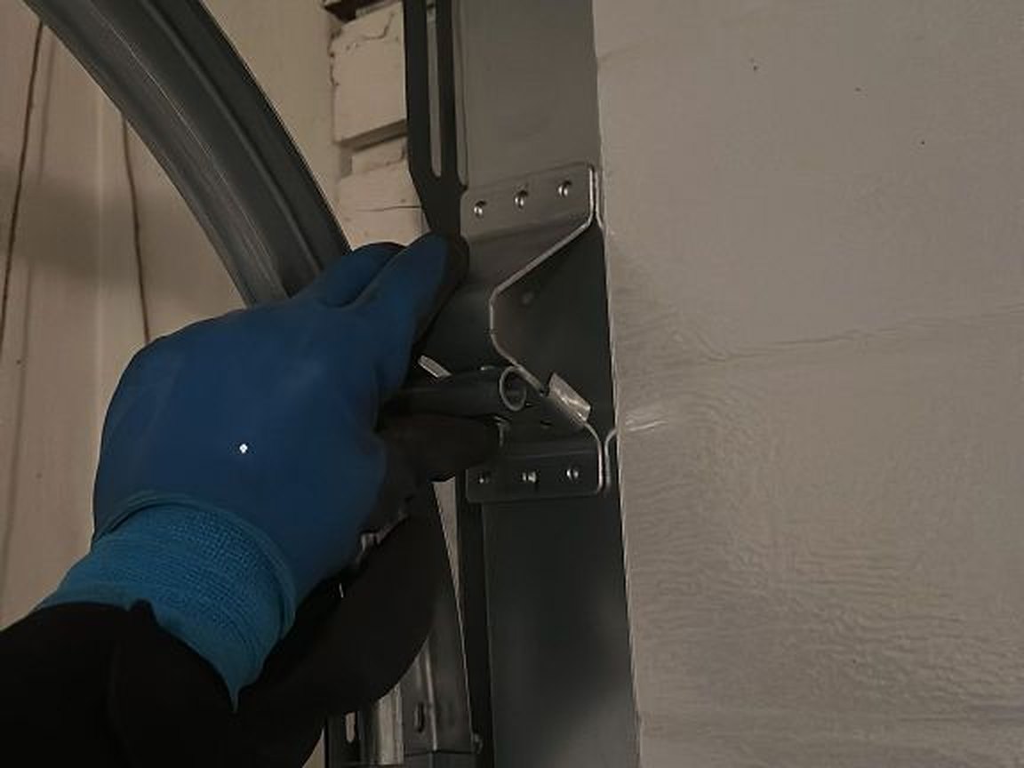 Gloved hand holding the curved track steady at the flag bracket while the fixings are checked during a service visit