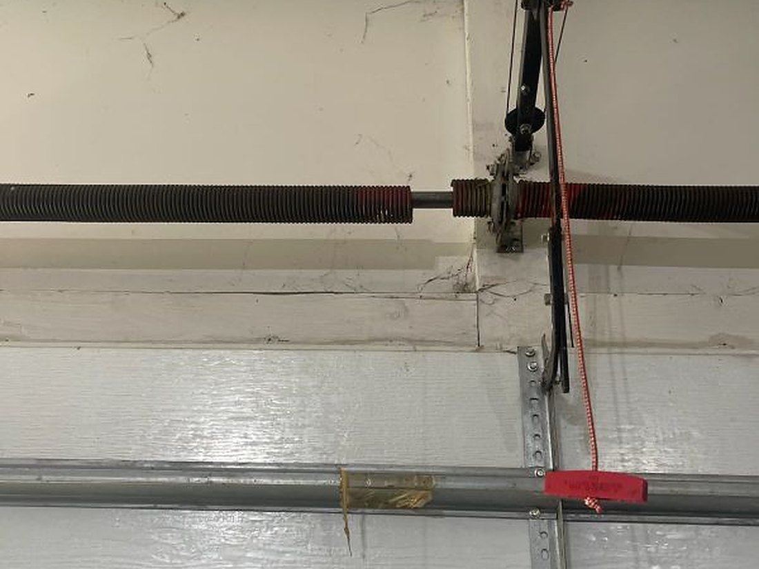 Torsion springs and shaft running across the header above a closed residential garage door, cable drums at each end and the emergency release cord hanging below